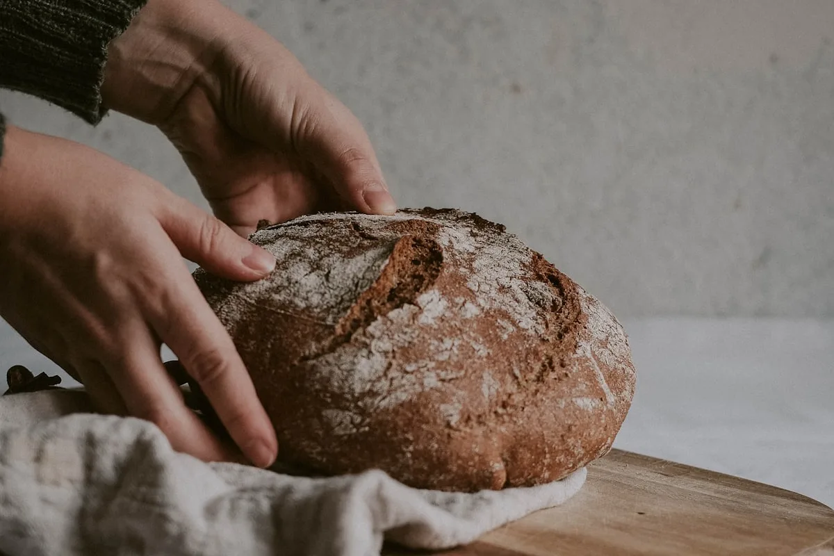 Mains tenant un pain au levain sur une planche en bois
